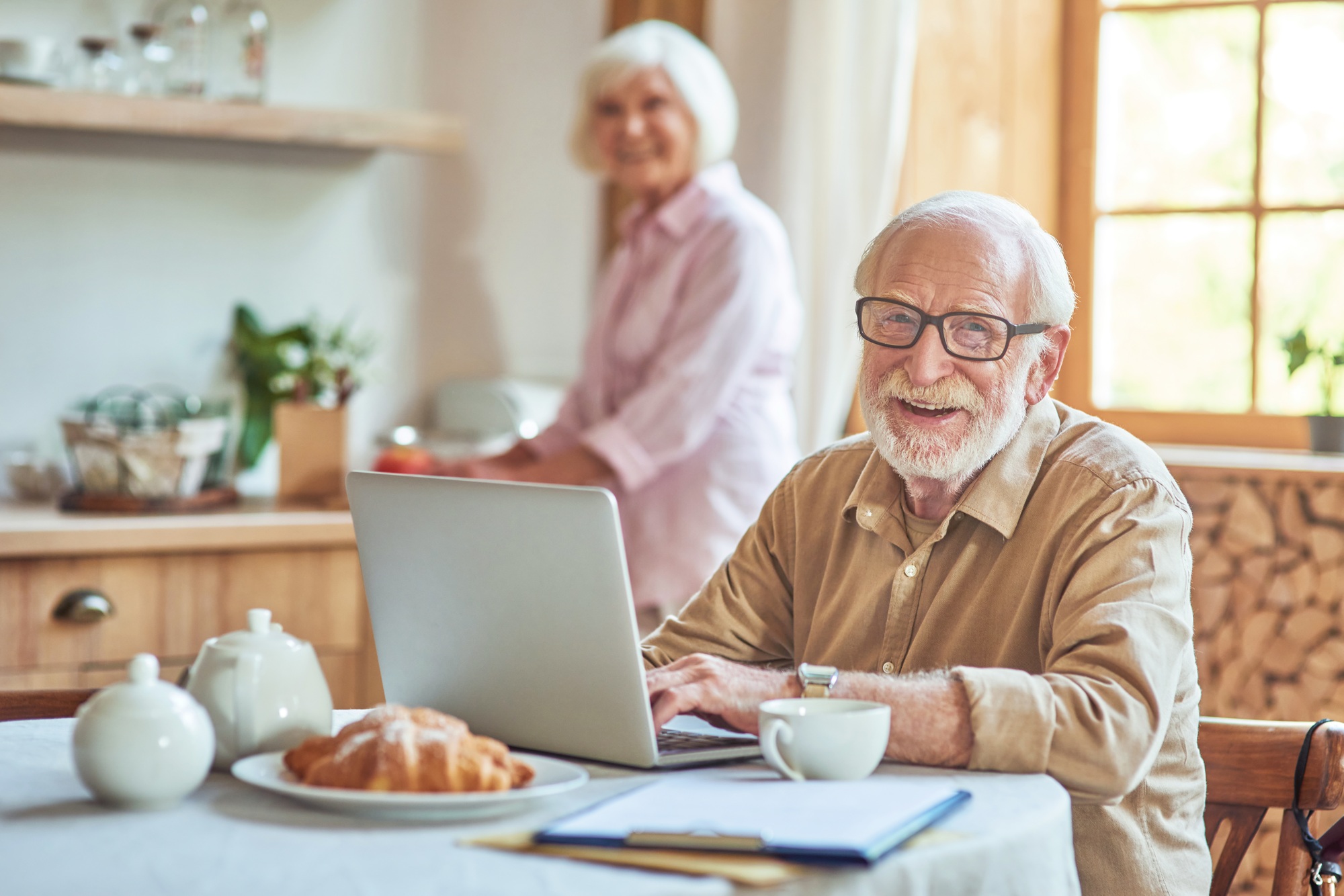 Smiling elderly spouses staying at the kitchen at their home