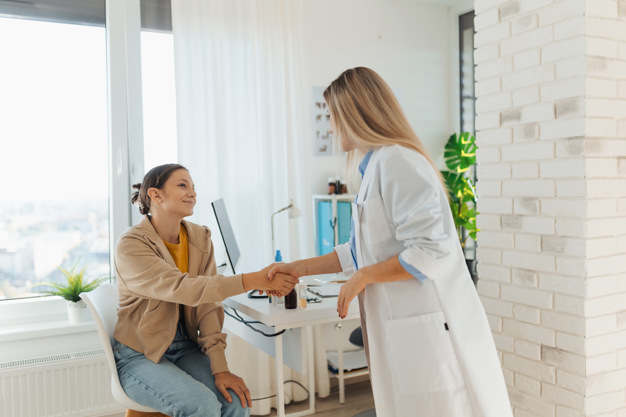 Teenage patient arriving at appointment with doctor, shaking hands with female pediatrician